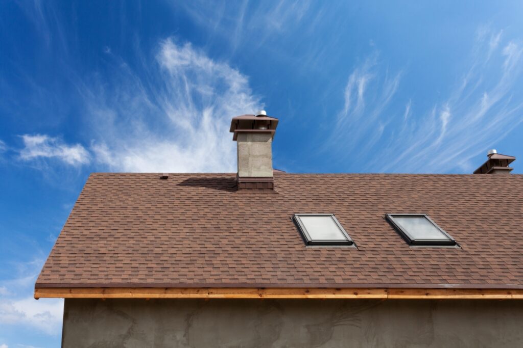 Roof with Brown Shingles and Skylights Against Blue Sky and Clouds